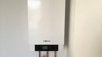 Ein moderner Heizkessel an einer weißen Wand, ausgestattet mit einem digitalen Display und Kupferrohren.