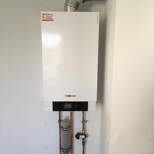 Ein moderner Heizkessel an einer weißen Wand, ausgestattet mit einem digitalen Display und Kupferrohren.