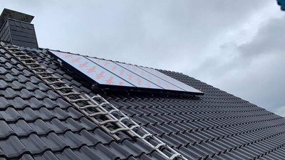 Ein Dach mit dunklen Ziegeln, auf dem eine Solaranlage montiert ist, während graue Wolken den Himmel bedecken.