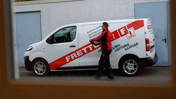 Ein Handwerker in schwarzer Arbeitskleidung trägt ein Werkzeug in der Hand, während er neben einem Firmenfahrzeug steht.
