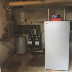 Ein moderner Heizkessel steht in einem Keller, umgeben von Rohren und zwei Zählern, die die Energieverbrauch anzeigen.
