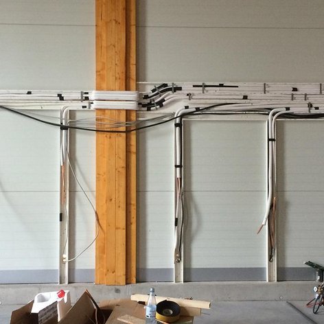 An einer Wand sind zahlreiche Kabel und Rohre sichtbar, die ordentlich verlegt und mit Kabelbindern gesichert sind.