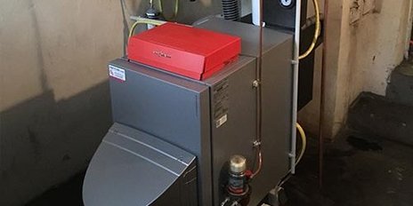 Eine moderne Heizungsanlage steht in einem Keller, mit einem roten Deckel und verschiedenen Rohren, die an die Wand angeschlossen sind.