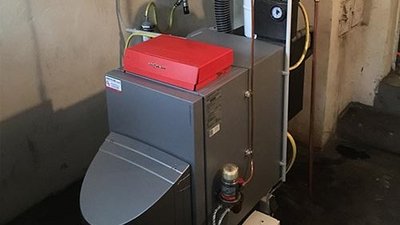 Eine moderne Heizungsanlage steht in einem Keller, mit einem roten Deckel und verschiedenen Rohren, die an die Wand angeschlossen sind.