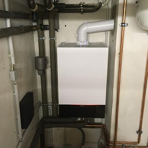 Eine moderne Heizungsanlage ist an der Wand montiert, umgeben von Rohren und Leitungen in einem technischen Raum.