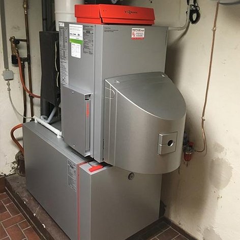 Eine moderne Heizungsanlage in einem Keller, die mit grauem Metall verkleidet ist und eine orangefarbene Abdeckung hat.