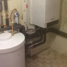 Ein Heizungsraum mit einem großen, runden Warmwasserspeicher und zahlreichen Rohren, die an die Wände angeschlossen sind.
