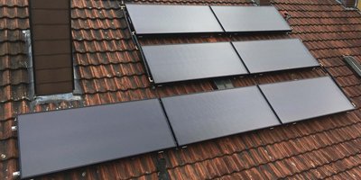 Auf einem Dach sind mehrere Solarpanels installiert, die auf den roten Ziegeln montiert sind und die Sonne reflektieren.
