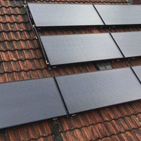 Auf einem Dach sind mehrere Solarpanels installiert, die auf den roten Ziegeln montiert sind und die Sonne reflektieren.